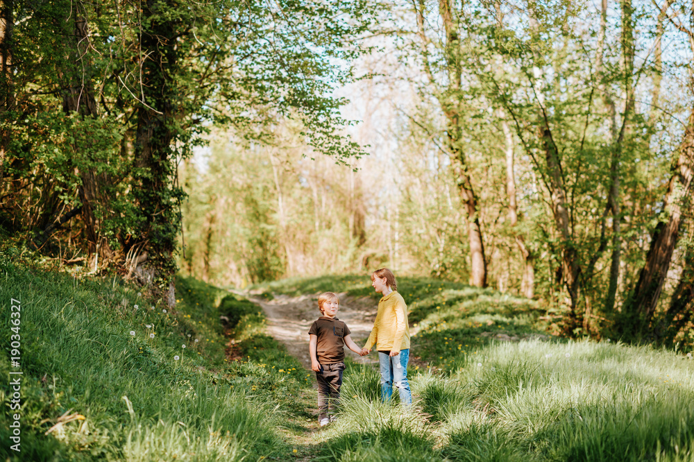 Two funny kids playing together in spring forest, little brother and sister enjoying nice walk in woods Two funny kids playing together in spring forest, little brother and sister enjoying nice walk in woods