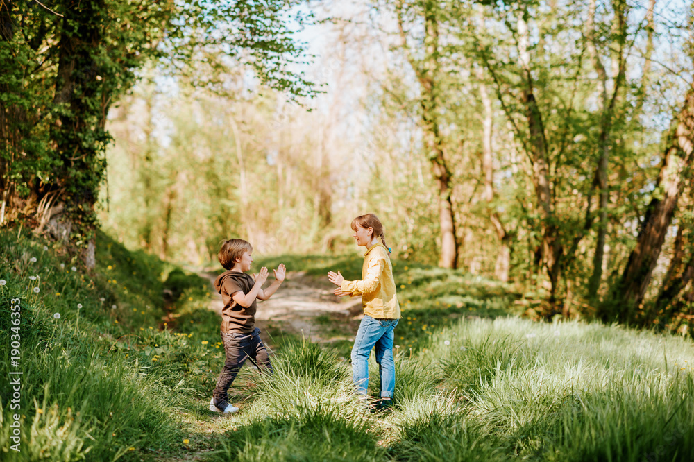 Fototapeta premium Two funny kids playing together in spring forest, little brother and sister enjoying nice walk in woods