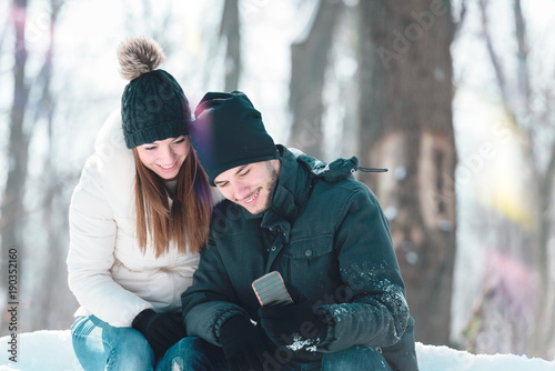 Smiling young couple in snow covered park looking at smartphone