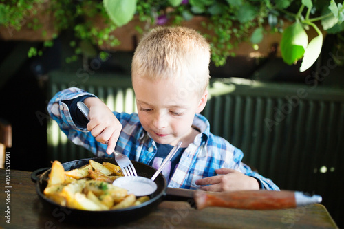 Cute healthy kid boy eats potatoes sitting in nursery cafe. Happy child eating  organic and vegan food in restaurant. Childhood.