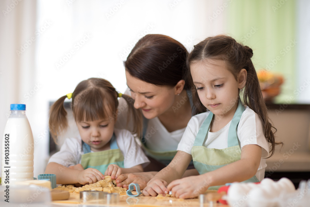 Happy loving family mother and daughters are preparing bakery together. Mom and children are cooking cookies and having fun in the kitchen. Homemade food and little helpers. Happy loving family mother and daughters are preparing bakery together. Mom and children are cooking cookies and having fun in the kitchen. Homemade food and little helpers.