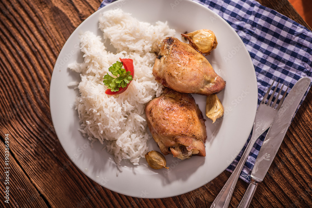 chicken tights upper leg on white plate with rice on wood table. 