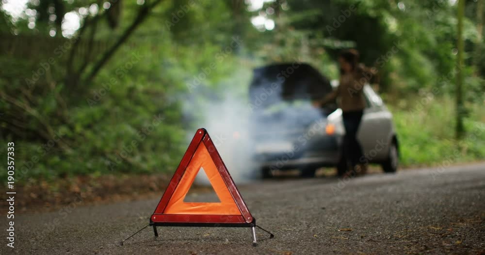 4K Stranded woman with broken down car phoning for assistance on quiet country road. Red warning triangle in foreground. Slow motion.