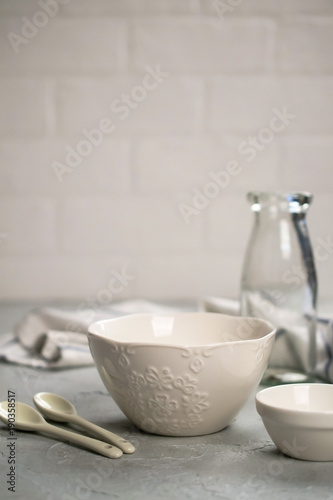 Simple home kitchen still life on a background of light walls on a  gray concrete table. Set of Porcelain Dishes and glass bottle. Kitchen Utensil