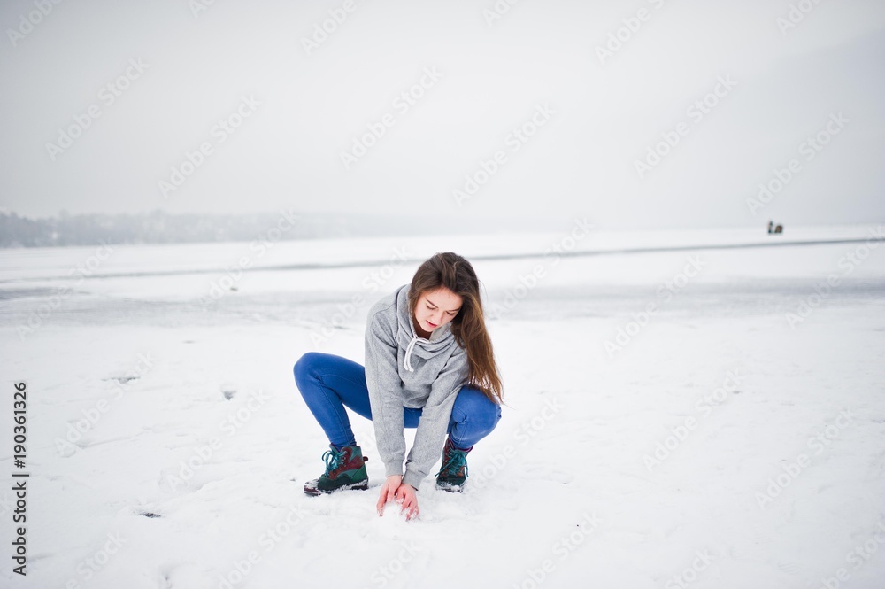 Funny girl wear on hoody sweater and jeans, at frozen lake in winter day.