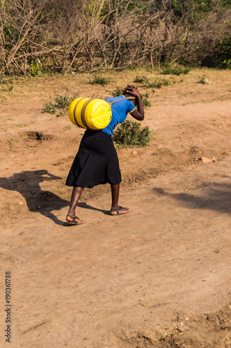 Masai woman carrying a can of water on her back in the savannah of Maasai Mara in North West Kenya