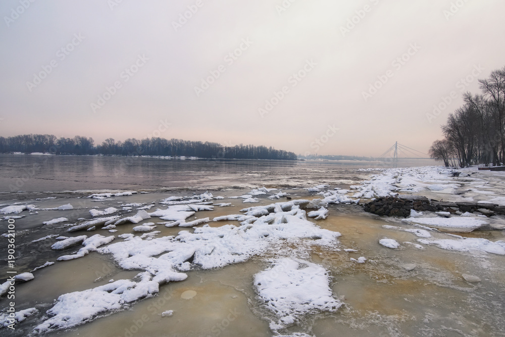 Winter morning view to the Dnipro River in winter. After a cold snap came a thaw. Ice on the river quickly melts and already water is clearly visible. Kyiv, Ukraine Winter morning view to the Dnipro River in winter. After a cold snap came a thaw. Ice on the river quickly melts and already water is clearly visible. Kyiv, Ukraine