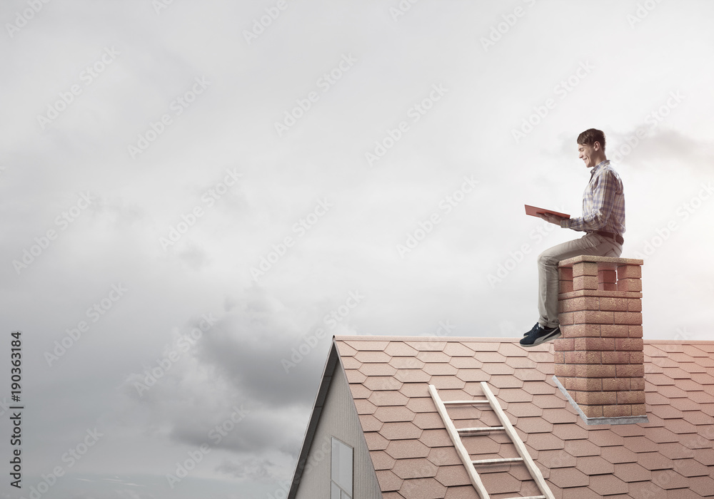 Handsome man on brick roof against cloud scape reading book Handsome man on brick roof against cloud scape reading book