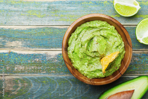 Green guacamole with  ingredients avocado, lime and nachos on wooden vintage table top view. Traditional mexican food.