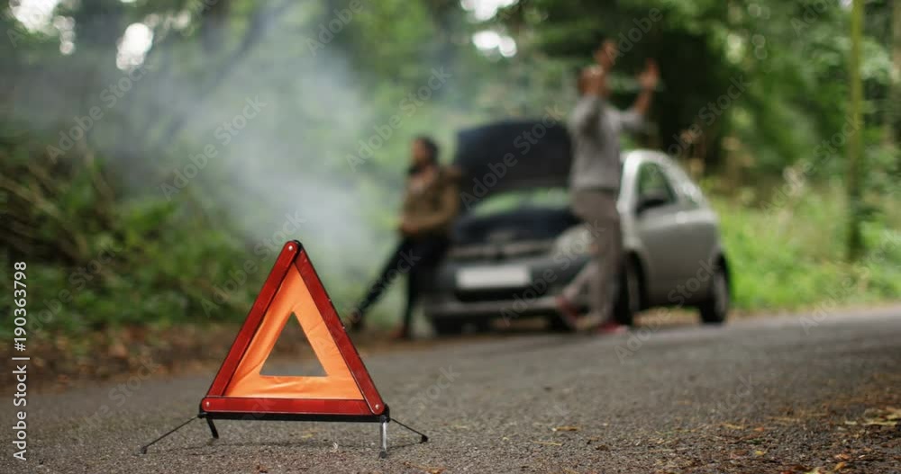 4K Stranded couple arguing in front of broken down car on quiet country road. Red warning triangle in foreground. Slow motion.