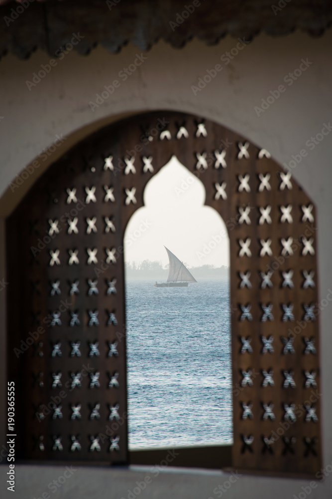 Traditional dhow boat sailing on the sea, seen through the window at sunset, Zanzibar