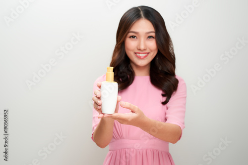 Smiling young asian woman showing skincare product.