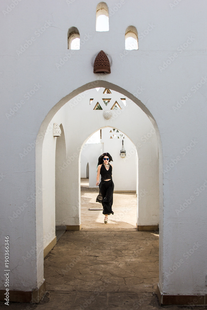 attractive young woman in sunglasses looking at camera while walking at white building in Egypt