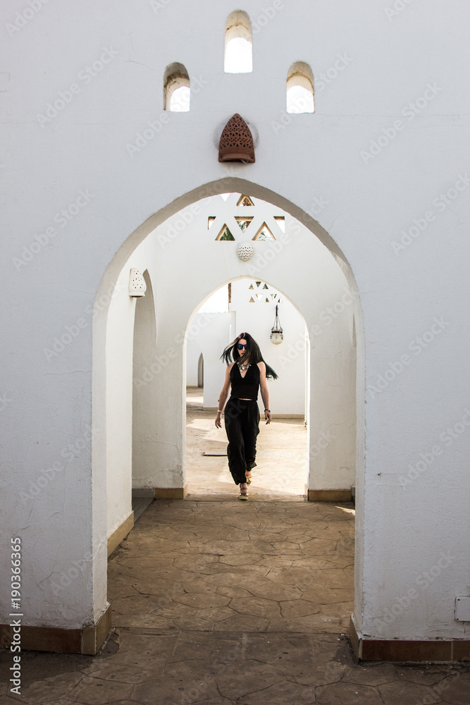 beautiful young woman in sunglasses looking at camera while walking at white building in Egypt