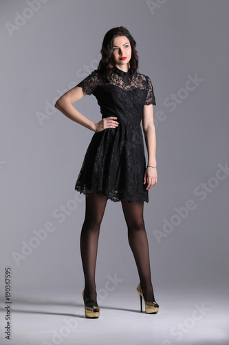 Woman in black dress showing model pose. Gray background. Photographie retouchee