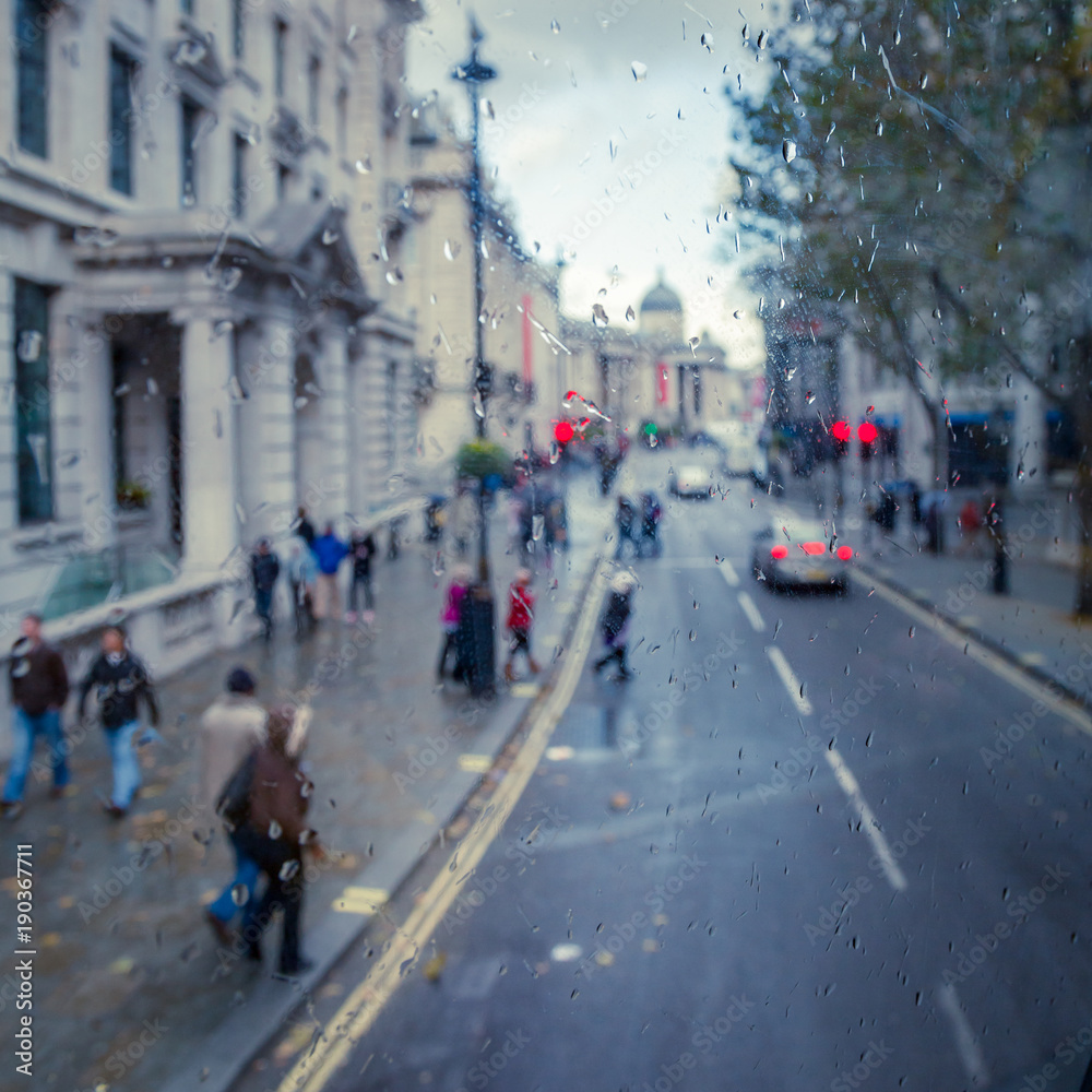 London city street scene through double decker bus window with rain drops toned