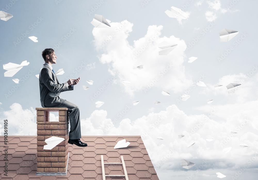 Man on brick roof send message with smartphone and paper planes Man on brick roof send message with smartphone and paper planes