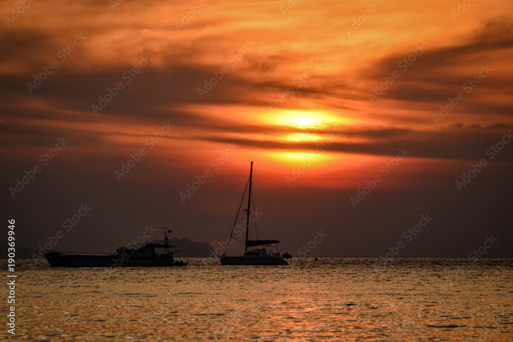sun rises behind sailing boat with dramatic colors