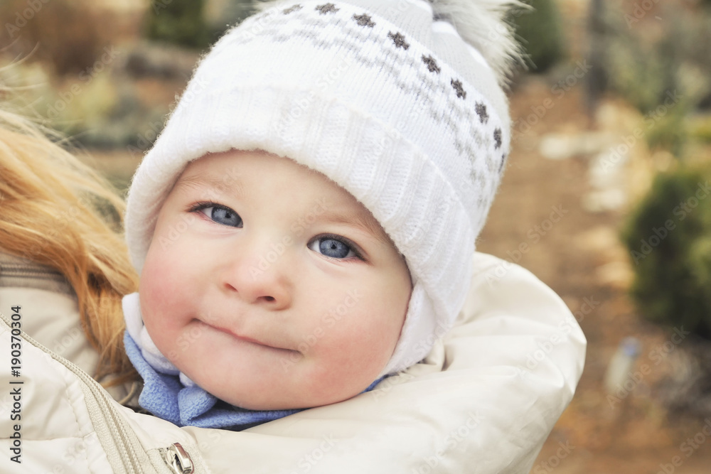 A child in a sling at the mother's under a jacket, a portrait of a baby in winter clothes A child in a sling at the mother's under a jacket, a portrait of a baby in winter clothes
