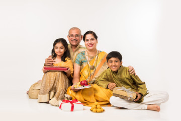 Indian kids with grandparents in traditional wear holding gifts, sweets and puja or pooja thali or taking selfie, isolated over white background

