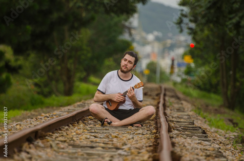 Young man on train tracks with his Ukulele playing some songs