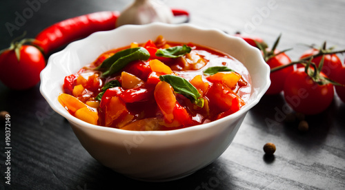 Delicious letcho with fresh vegetables in bowl on dark wooden background photo