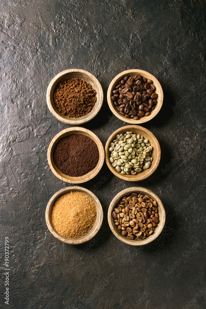 Variety of grounded, instant coffee, different coffee beans, brown sugar in wooden bowls in row over dark texture background. Top view, space