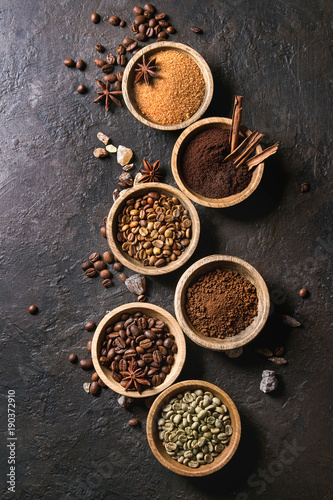 Variety of grounded, instant coffee, different coffee beans, brown sugar, spices in wooden bowls over dark texture background. Top view, space