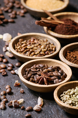 Variety of grounded, instant coffee, different coffee beans, brown sugar, spices in wooden bowls over dark texture background. Close up