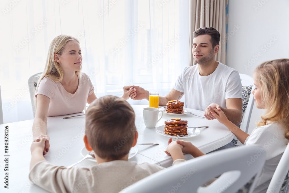 christian family praying before breakfast and holding hands christian family praying before breakfast and holding hands