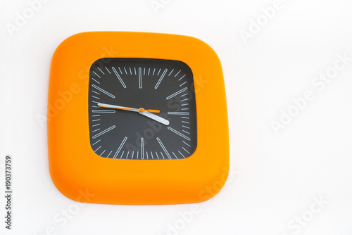 orange plastic clock on white wall, evening time