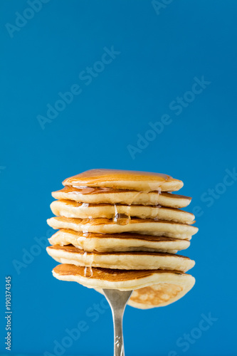 Stack of pancakes with honey decorated sweet cherry pinned on a fork on blue background