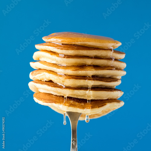 Stack of pancakes with honey decorated sweet cherry pinned on a fork on blue background