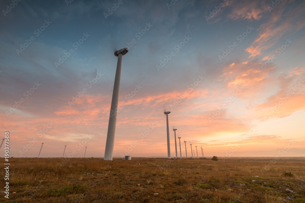 Fototapeta premium Wind turbines against red, blue and orange sunrise