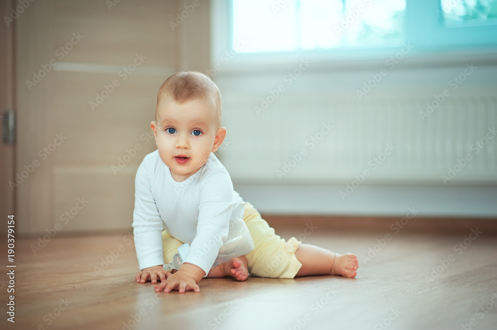 Adorable little baby sitting in bedroom on the floor with bottle with milk or water and laughing. Infant Childhood Kids People concepts. Cozy home with children Lifestyle Adorable little baby sitting in bedroom on the floor with bottle with milk or water and laughing. Infant Childhood Kids People concepts. Cozy home with children Lifestyle