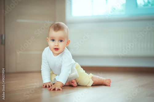 Adorable little baby sitting in bedroom on the floor with bottle with milk or water and laughing. Infant Childhood Kids People concepts. Cozy home with children Lifestyle
