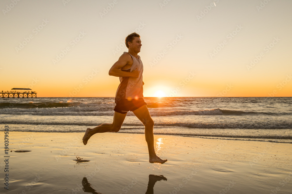  young dynamic athlete runner man with fit strong body training on Summer sunset beach running barefoot in sport healthy and fitness concept