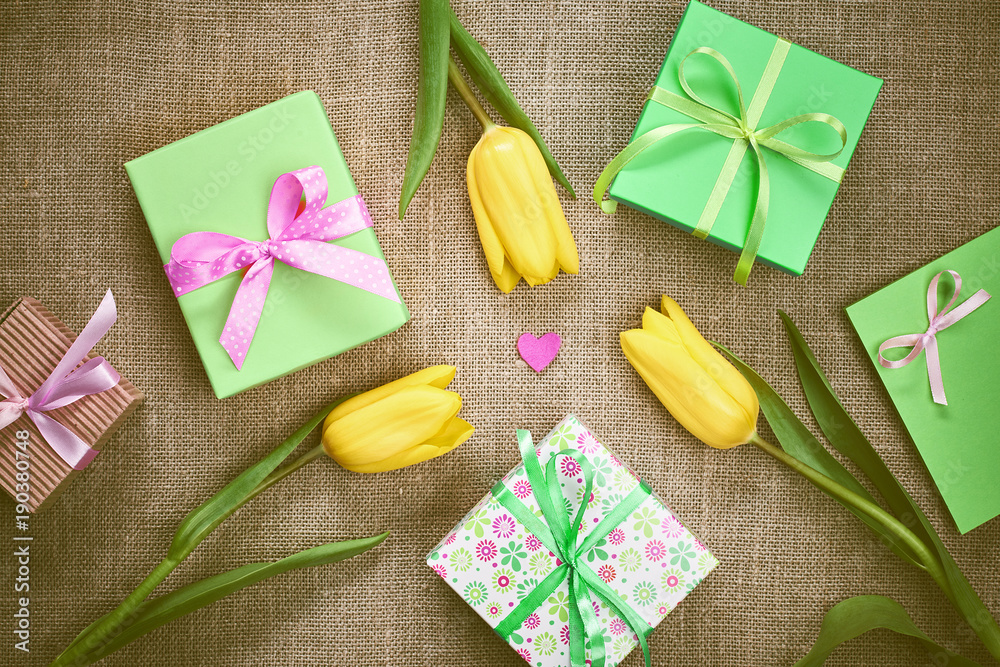 Tulips, Gift boxes on sackcloth. Mothers Day background. Beautiful Spring yellow tulips, presents, hearts. Creative Romantic Style. Colorful holiday. Art