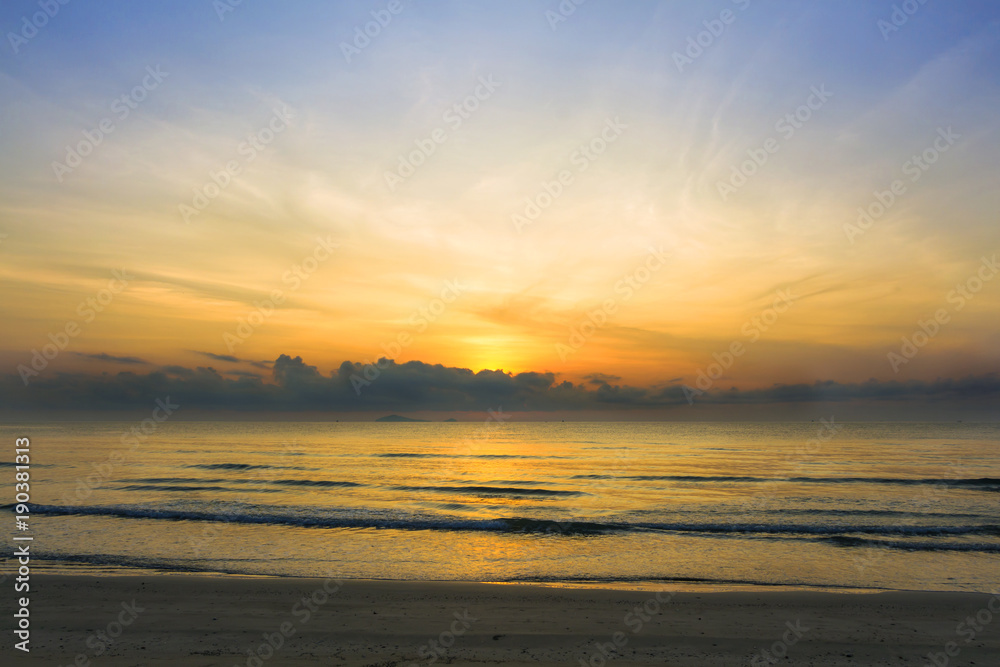 Sunrise over the tropical seacoast beach. The wave of seawater up the beach and waves slowly splashing on the sand.