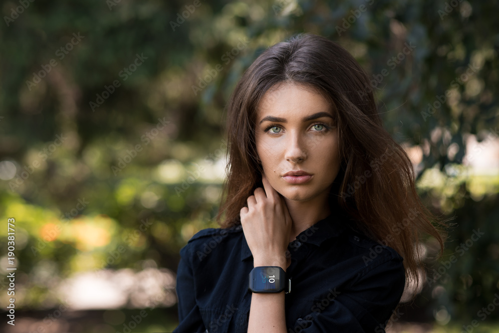 Portrait of a beautiful girl on the street with a hand with a clock at the face. Smart watch..