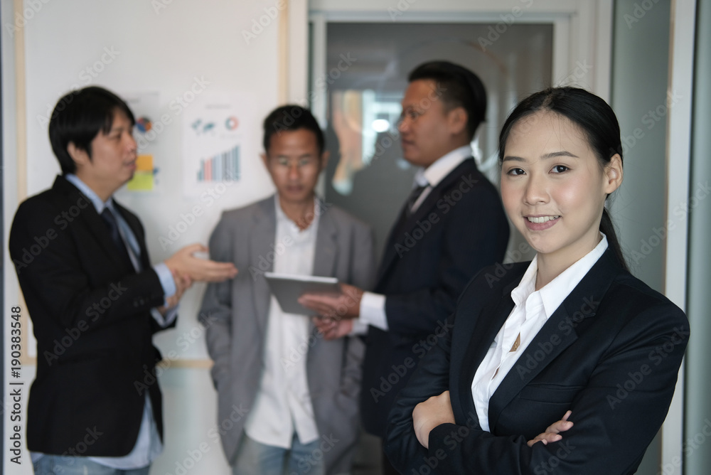 asian businesswoman smiling at camera while colleagues have meeting at office. businessman working with co worker team asian businesswoman smiling at camera while colleagues have meeting at office. businessman working with co worker team