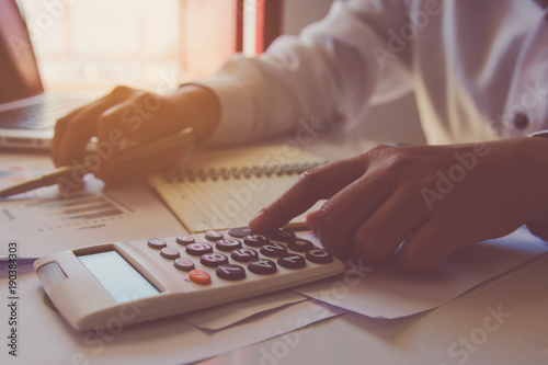 Man hand using a financial calculator with writing make note and Financial data analyzing on desk at home