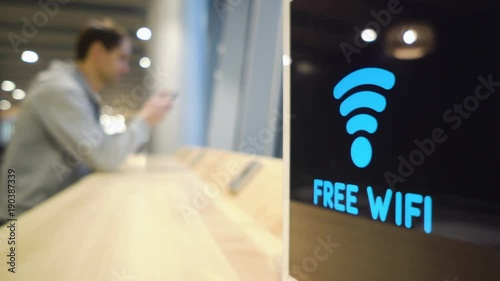 young man uses a phone on a background of a Free Wifi Signal Sign flashes on display in a cafe
