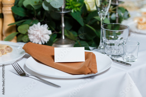Wedding table setting with blank guest card, napkin, succulent and dish on a wooden plate. Rustic decor in brown tones