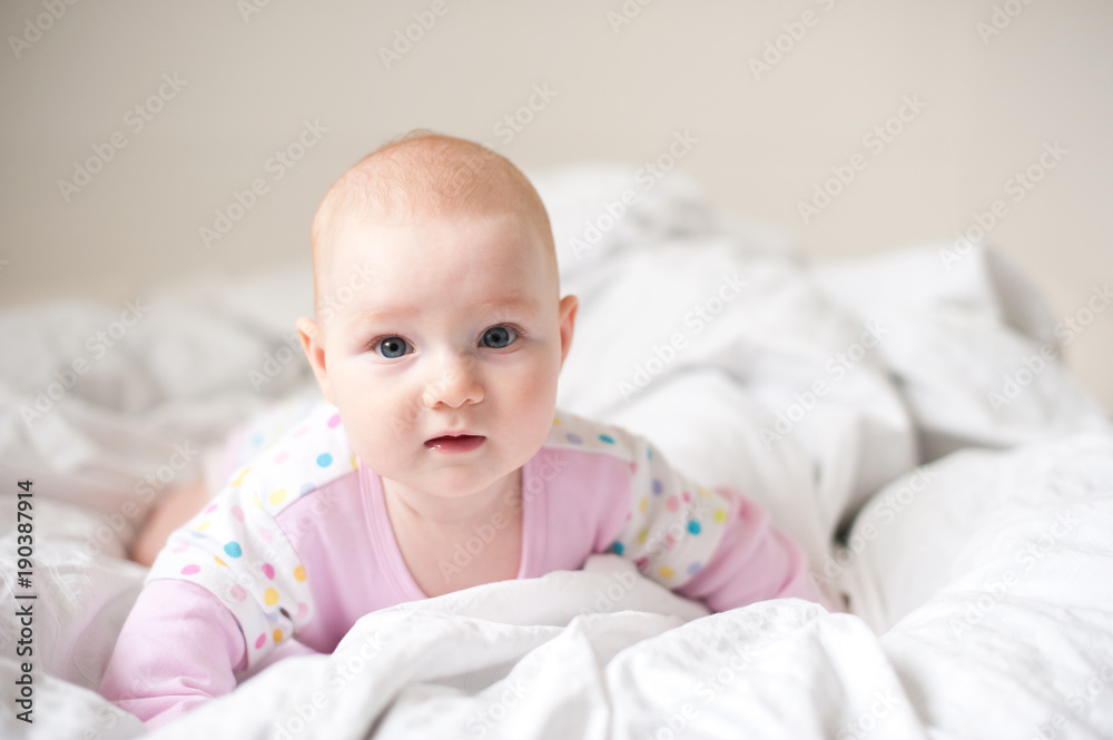 Baby girl in pink t-shirt on white bed