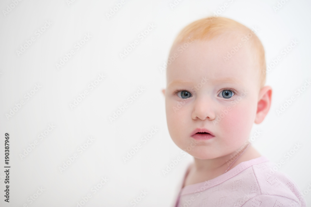 Baby girl in pink body looks at the camera on the white background