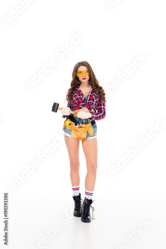beautiful girl in goggles and gloves with tool belt holding hammer, isolated on white