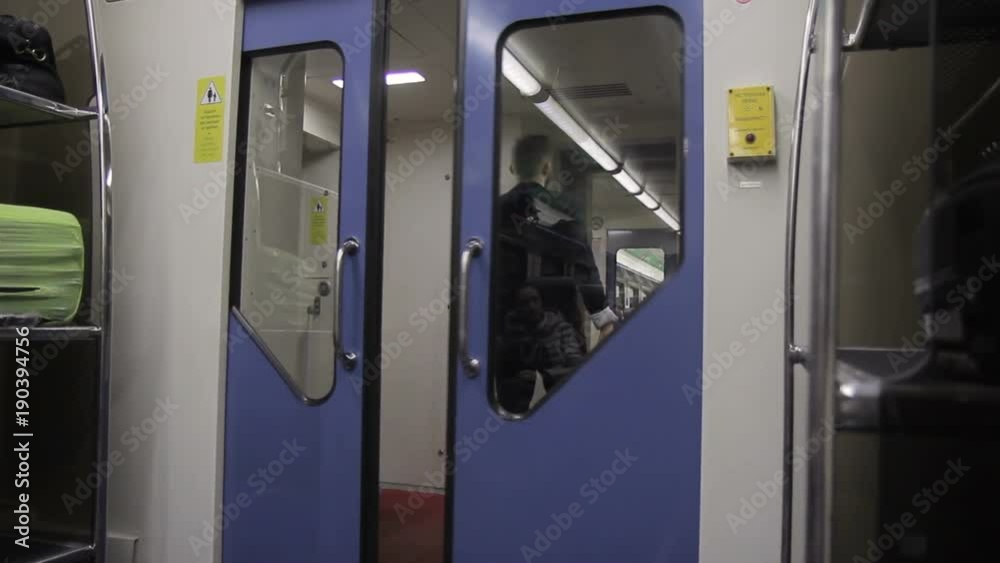 Businessman is going out from the waggon to enclosed platform. Adult man in black suit is comes to the doors, opens it and keeps walking while traveling by train. Shelfs with luggage bags are there Businessman is going out from the waggon to enclosed platform. Adult man in black suit is comes to the doors, opens it and keeps walking while traveling by train. Shelfs with luggage bags are there