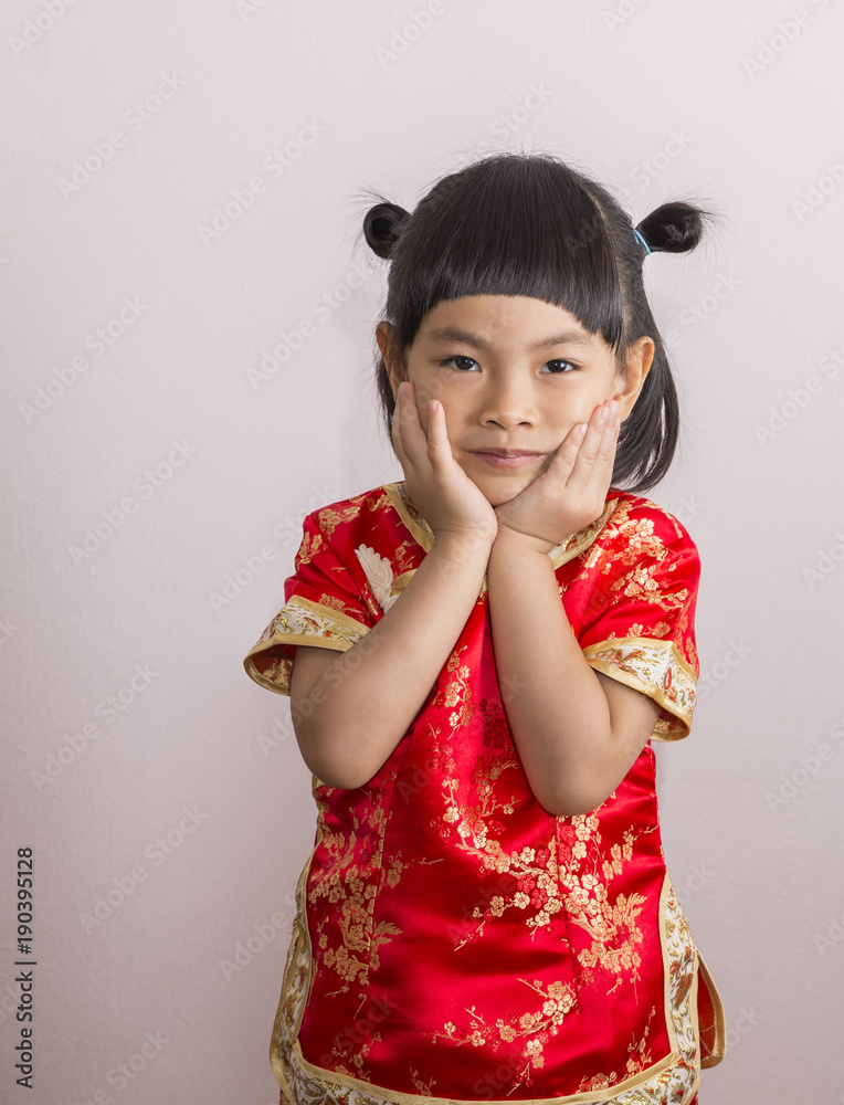 Adorable little girl in red Chinese dress for Chinese New Year theme. Little girl with two hand on cheek and  look at camera.