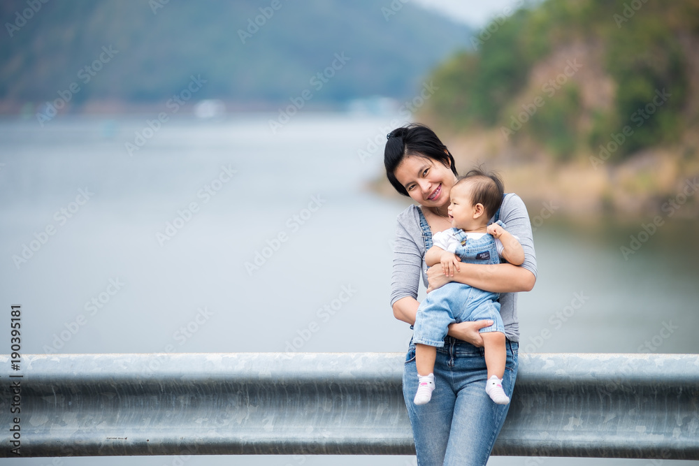 Asian mother showing her cute little girl smiling in her arms with blue lake in background.
